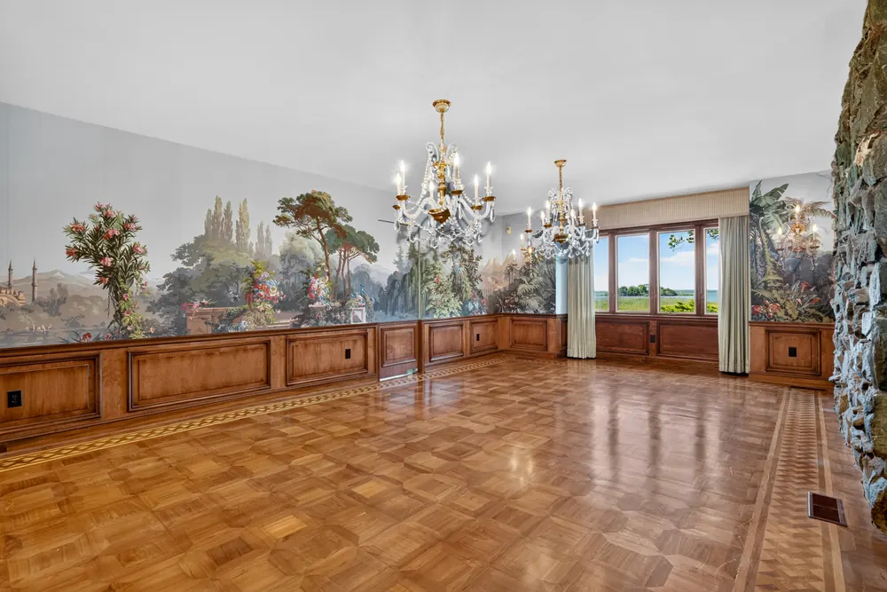 The formal dining room, with a scenic mural above wood wainscoting, two crystal chandeliers and windows facing the bay