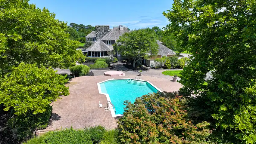 The pool and brick deck, framed by trees, with the house behind